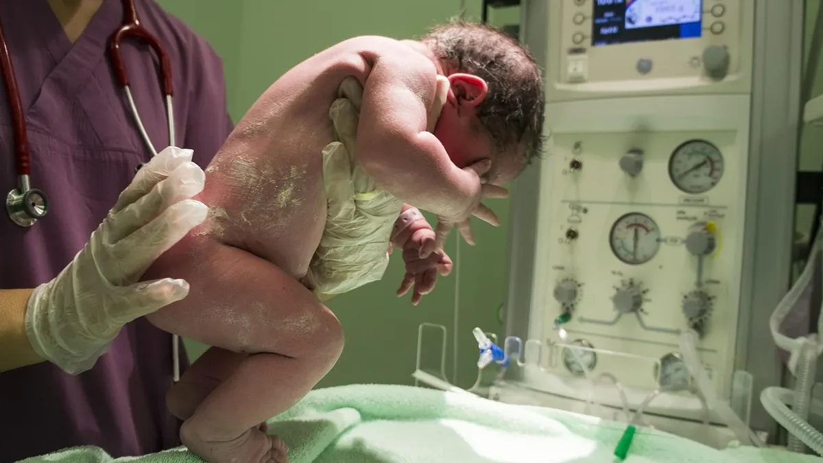 A newborn baby being held by a healthcare professional in a hospital setting.