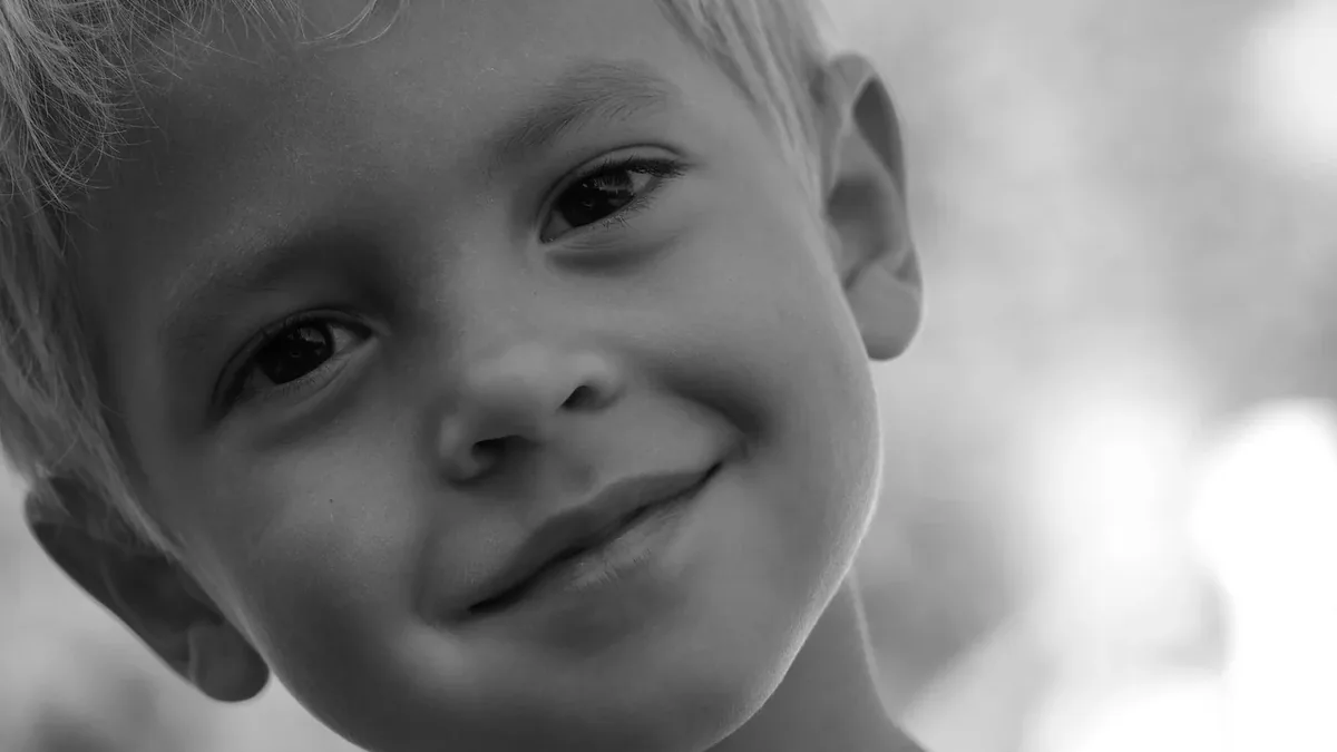 A close-up of a young boy's face, with his head tilted slightly to the left and a slight smile on his lips.