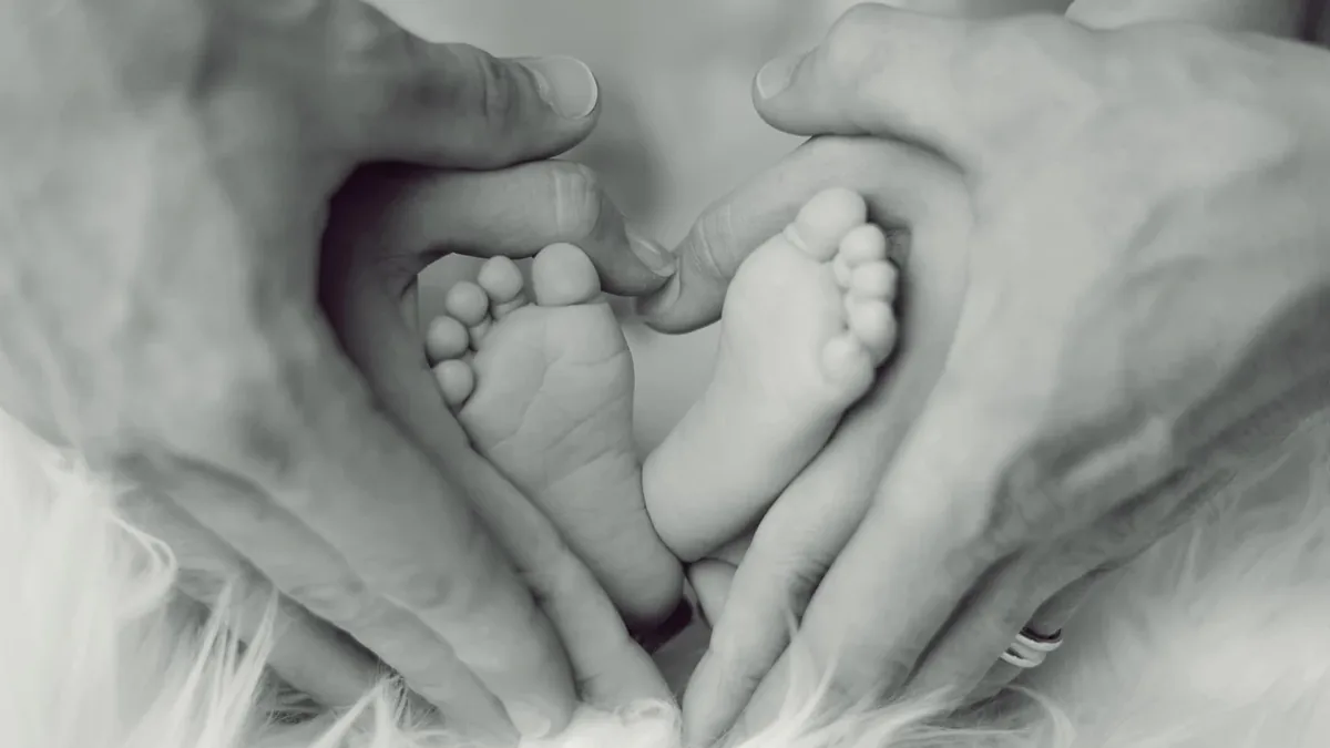 A pair of adult hands cradling a pair of baby feet, with the baby's toes curled up and the adults' fingers wrapped around the soles.